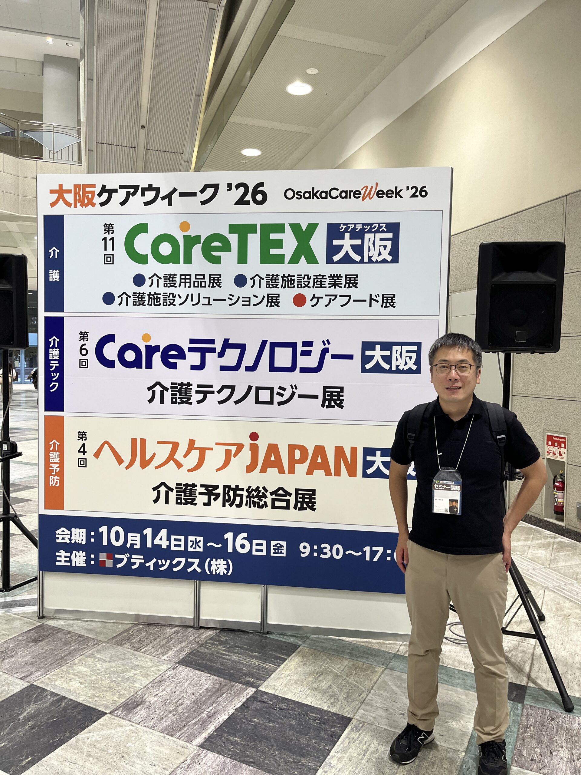 CareTEX大阪’26の会場看板の前に立つ八木大志